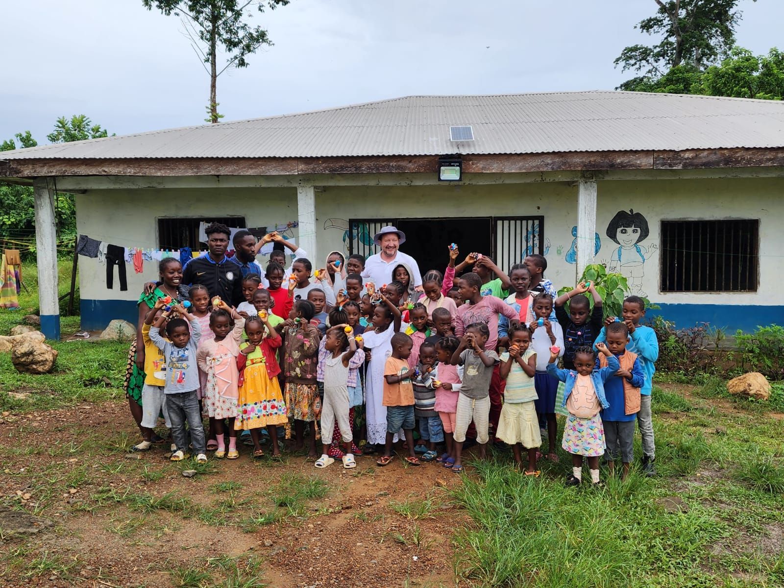 A large group of children and adults gathered outside a painted school building in Cameroon.
